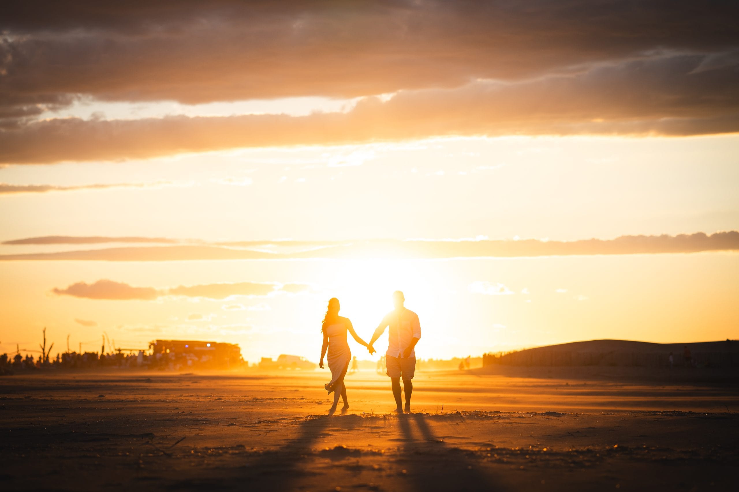 Couple holding hands and walking on a beach at sunset, silhouettes in golden light