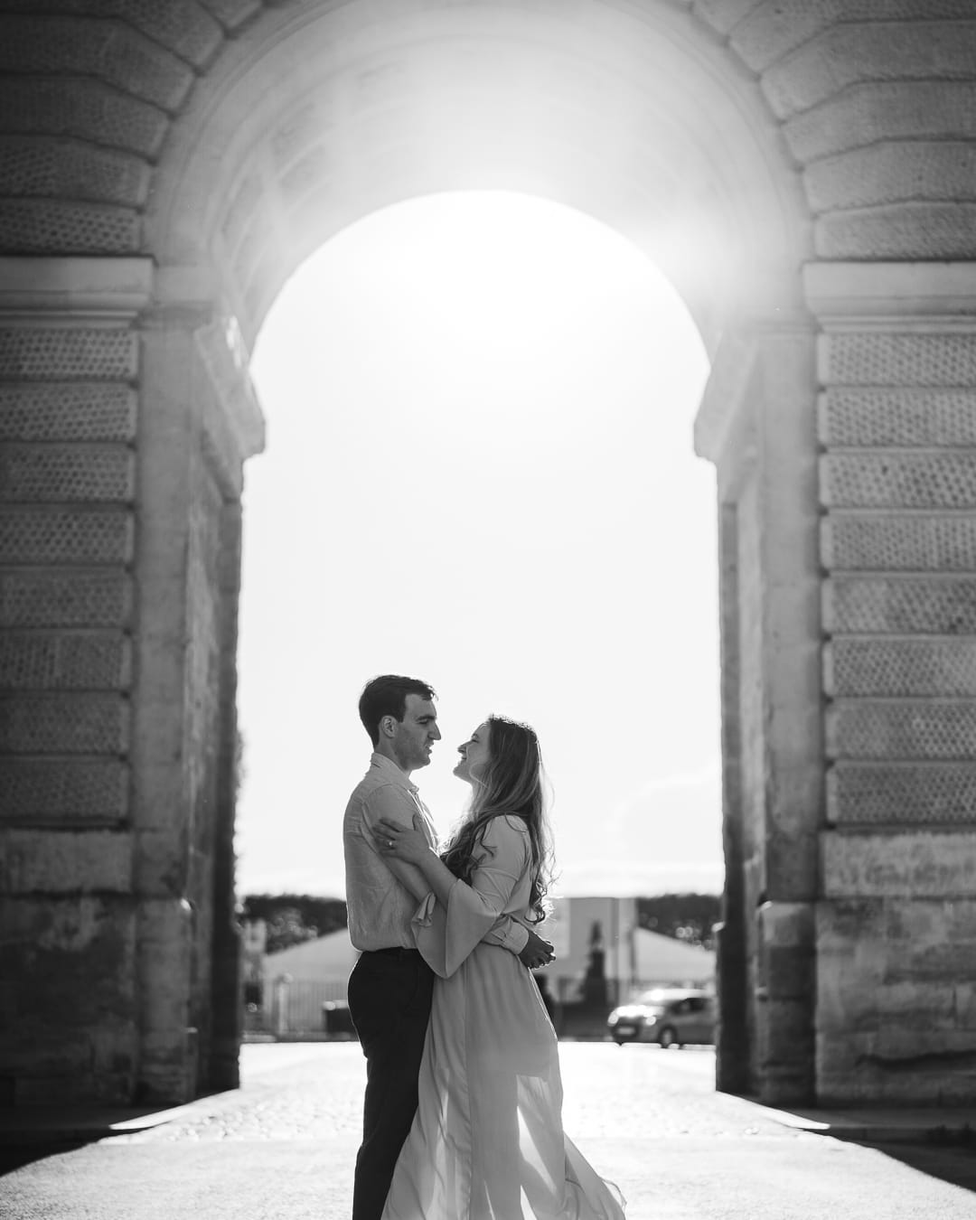 A couple embracing under the Arc de Triomphe gateway in Montpellier, backlit