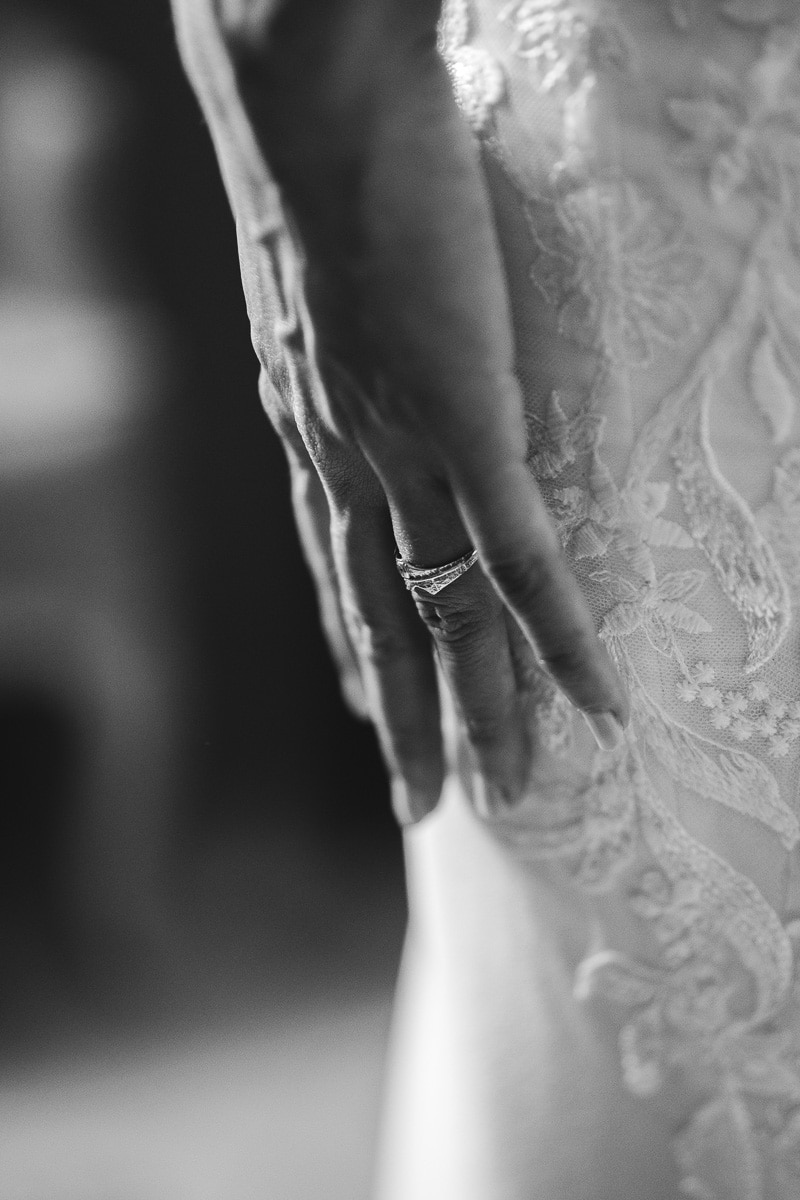 Close-up of the bride’s hand resting on her lace gown – an intimate and emotional detail captured with elegance, in the spirit of documentary and timeless wedding photography.