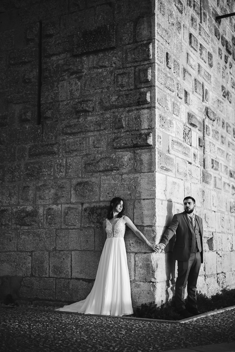 Bride and groom holding hands by the stone walls of the Tour Carbonnière near Aigues-Mortes in Occitanie – a timeless and emotional scene captured in natural light, true to documentary and timeless wedding photography.