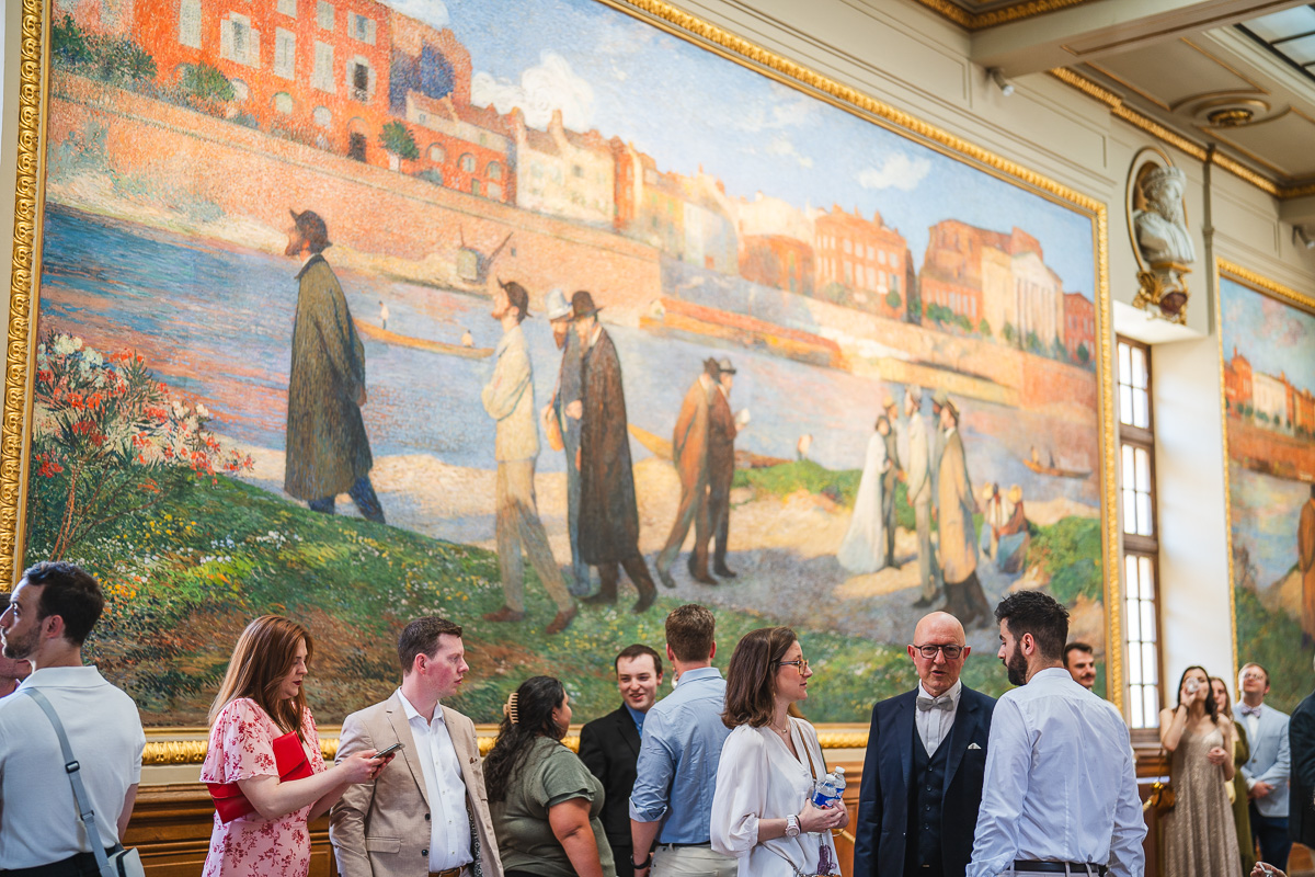 Perspective play inside the Capitole de Toulouse, historical paintings and guests in the foreground