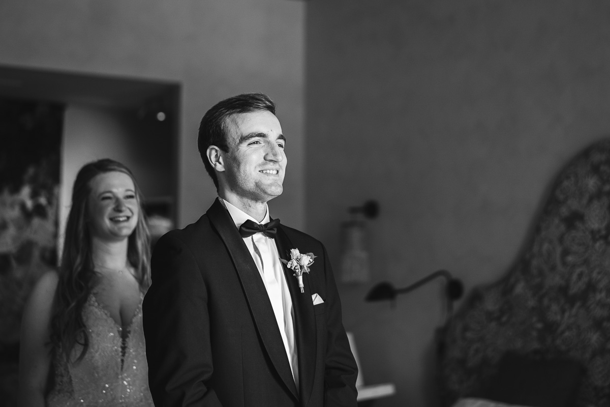 Black and white first look, the groom waiting with his back turned at La Bélonie, Halte en Cocagne