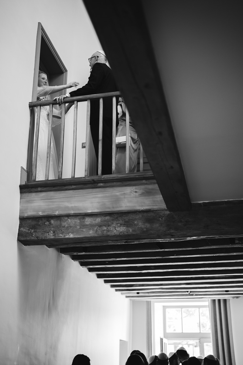View from the corridor looking up to the landing, the bride and her father in a doorframe at La Bélonie, Halte en Cocagne