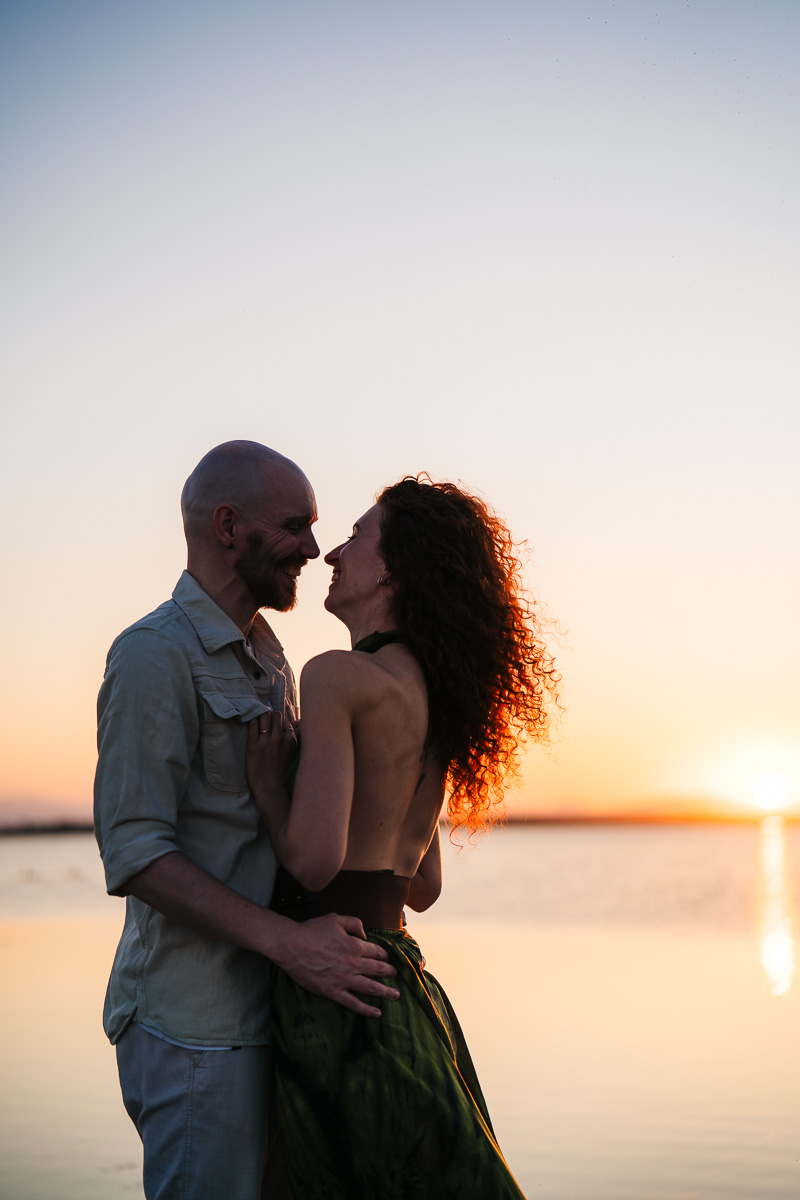 Couple standing face to face by the water at sunset, soft golden hour light