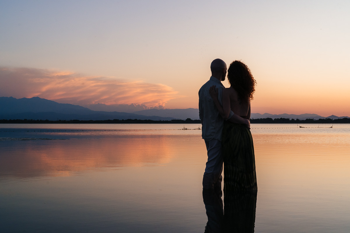 Couple at sunset ankle-deep in the Étang de Canet, Pyrénées-Orientales, Pyrenees mountains in the background