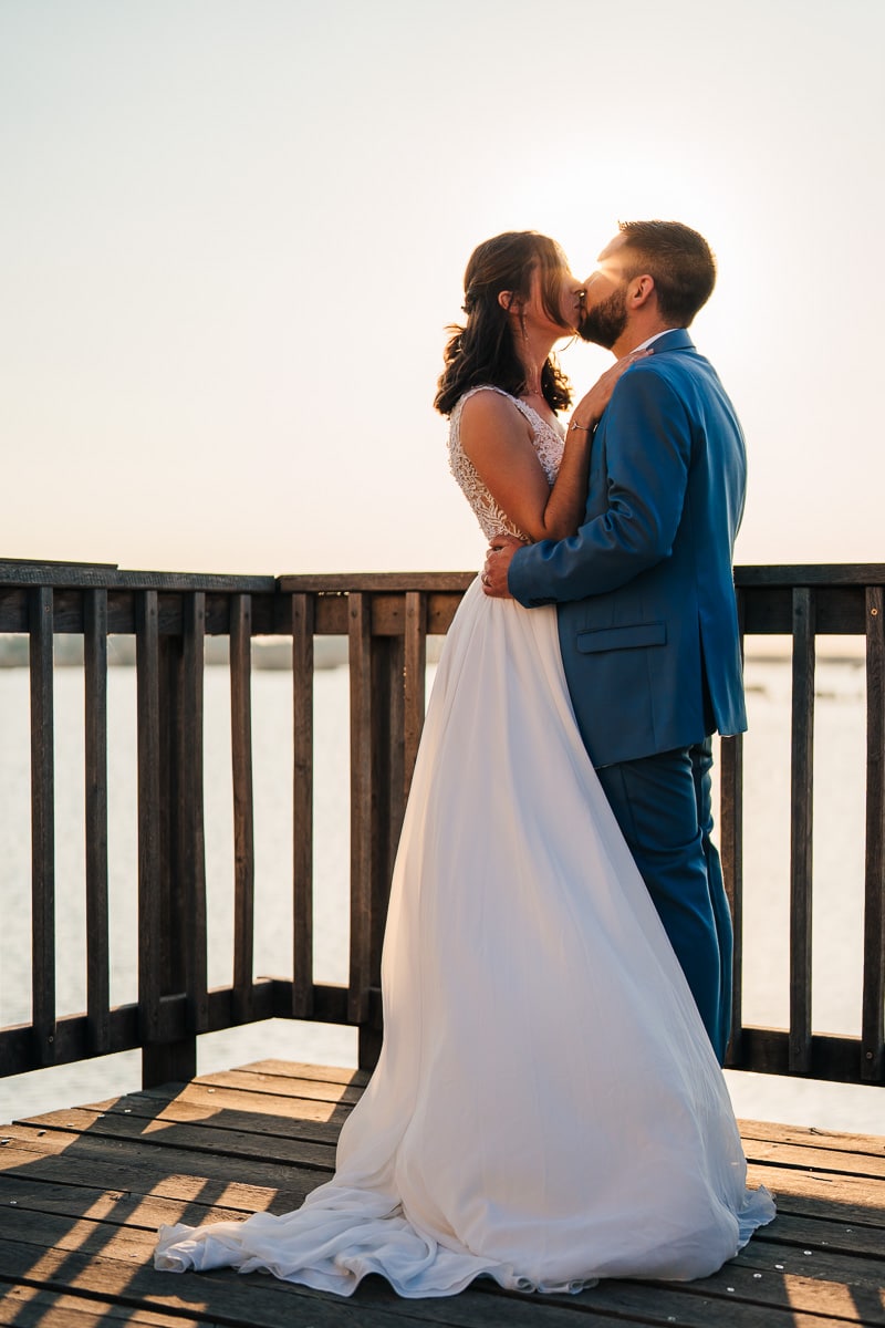 Married couple kissing on a wooden jetty in front of Camargue marshes at sunset backlit