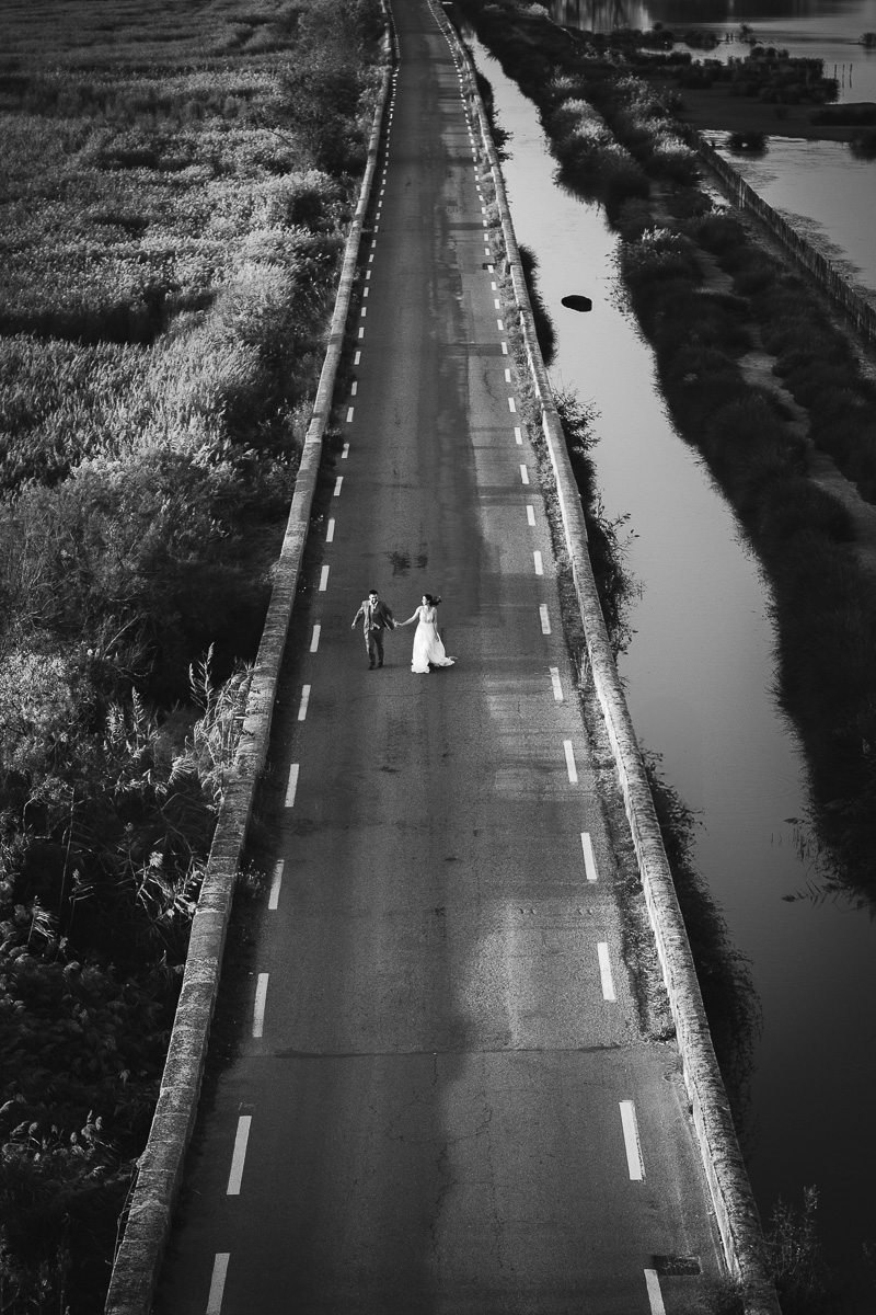 Married couple running on the road at the foot of Tour Carbonnière during a day after session, photo taken from above