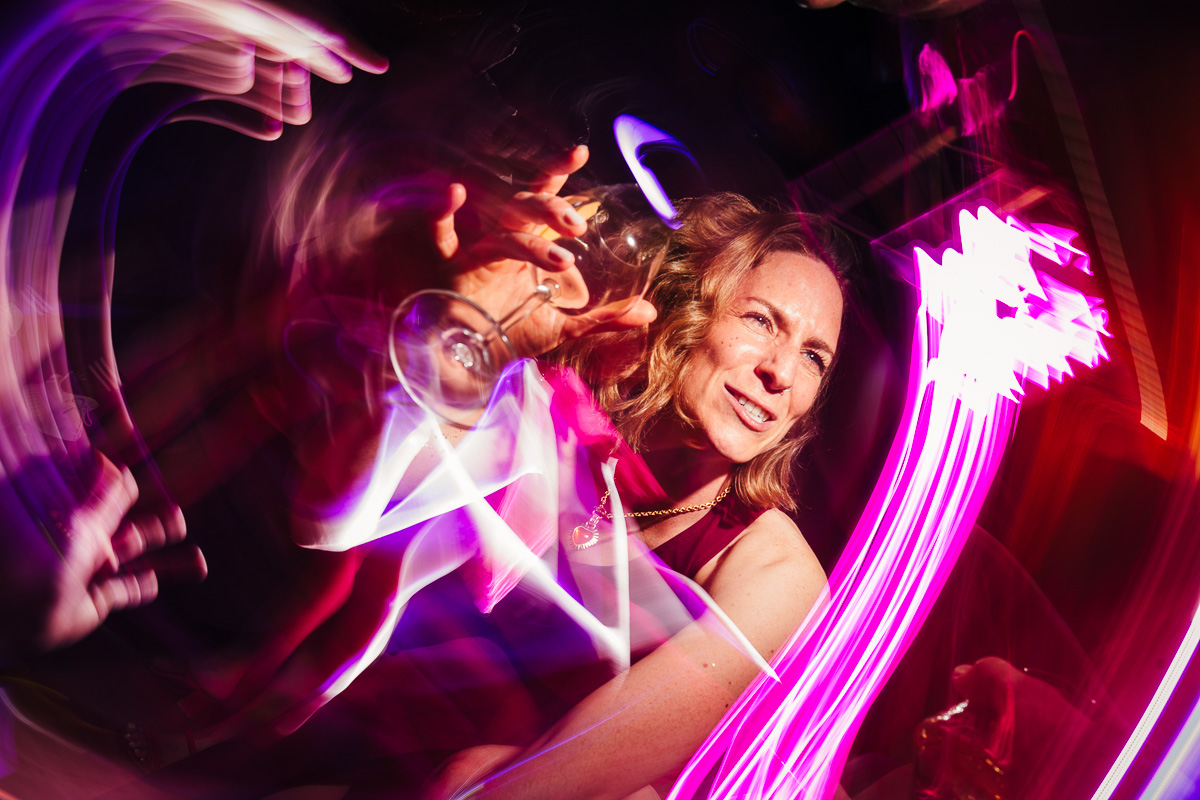 A smiling guest raising her glass on the dancefloor, surrounded by pink and red light trails
