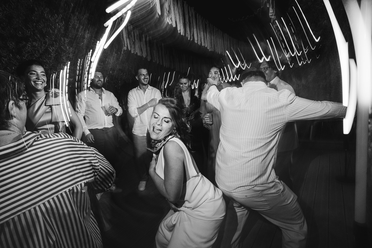 Guests dancing and laughing on the dancefloor of a wedding party, with light trails