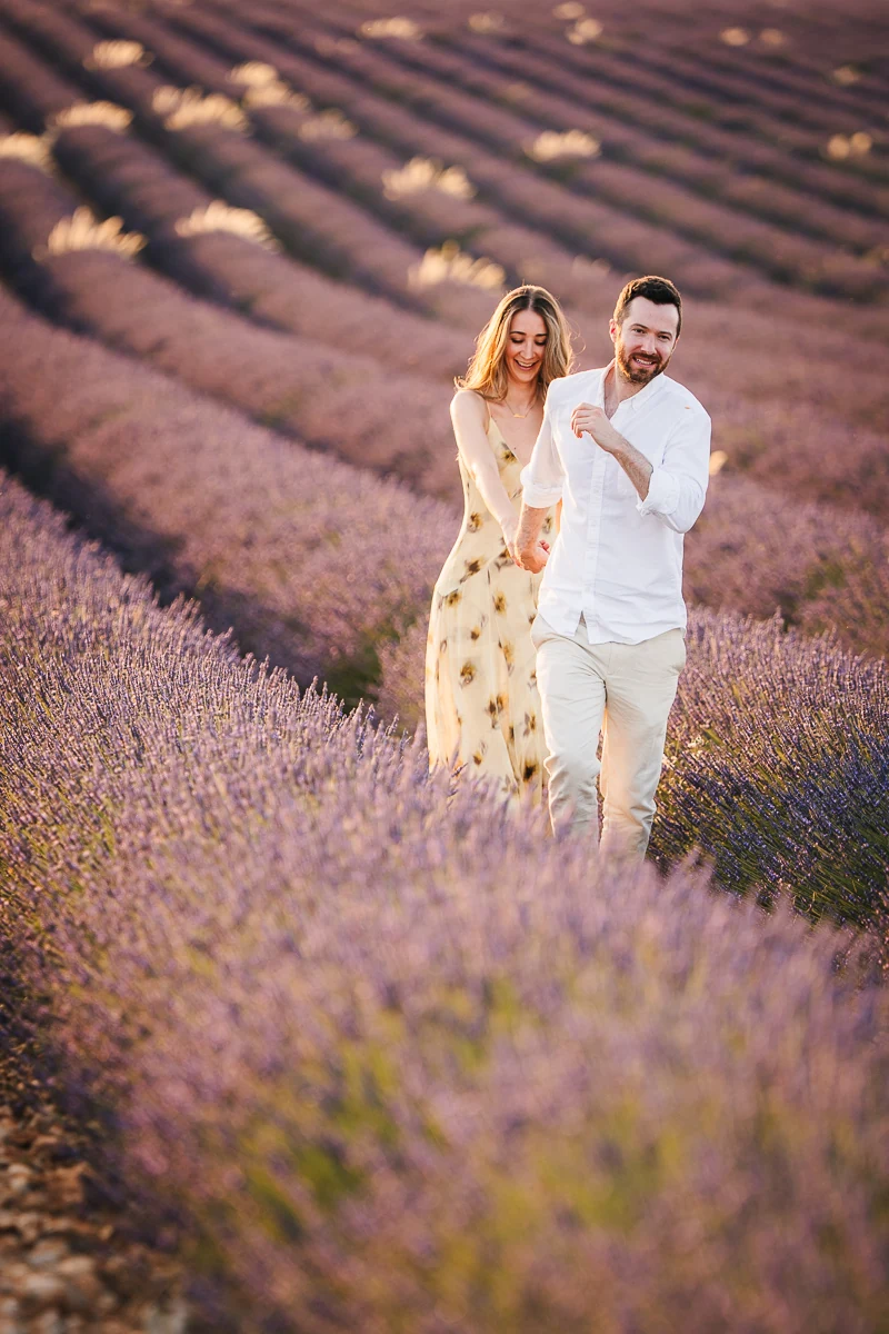 A couple walking toward the camera hand in hand, laughing, in a lavender field