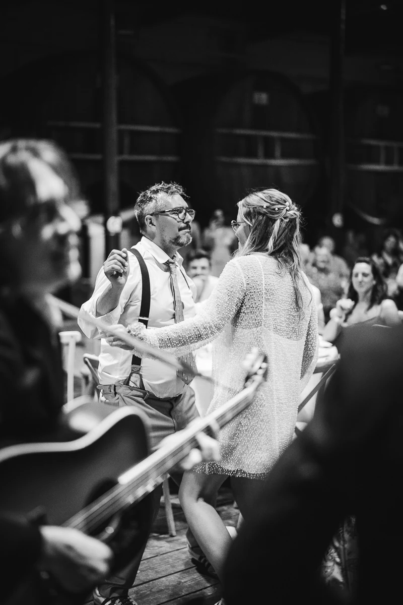 Black and white photo of a UK couple dancing among their guests with a live band playing

