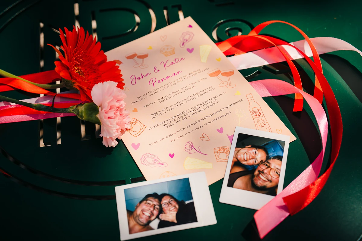 Wedding invitation with red flowers, ribbons and polaroid photos on a green table