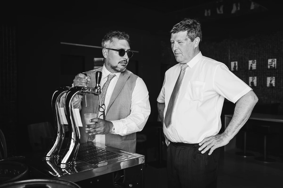 Black-and-white portrait of two men in white shirts standing in front of a beer tap
