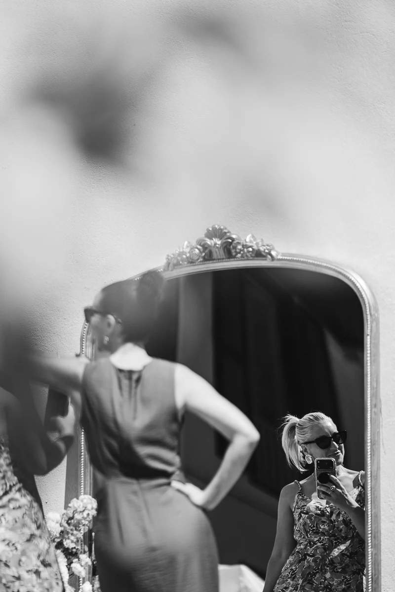 Black and white photo of the bride and guest taking photo in front of a mirror