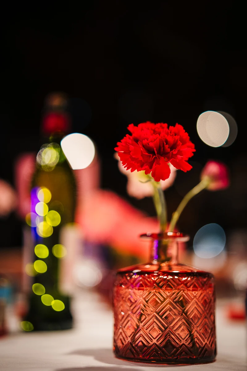 Red flower arrangement with candles and bottles on a table at dusk