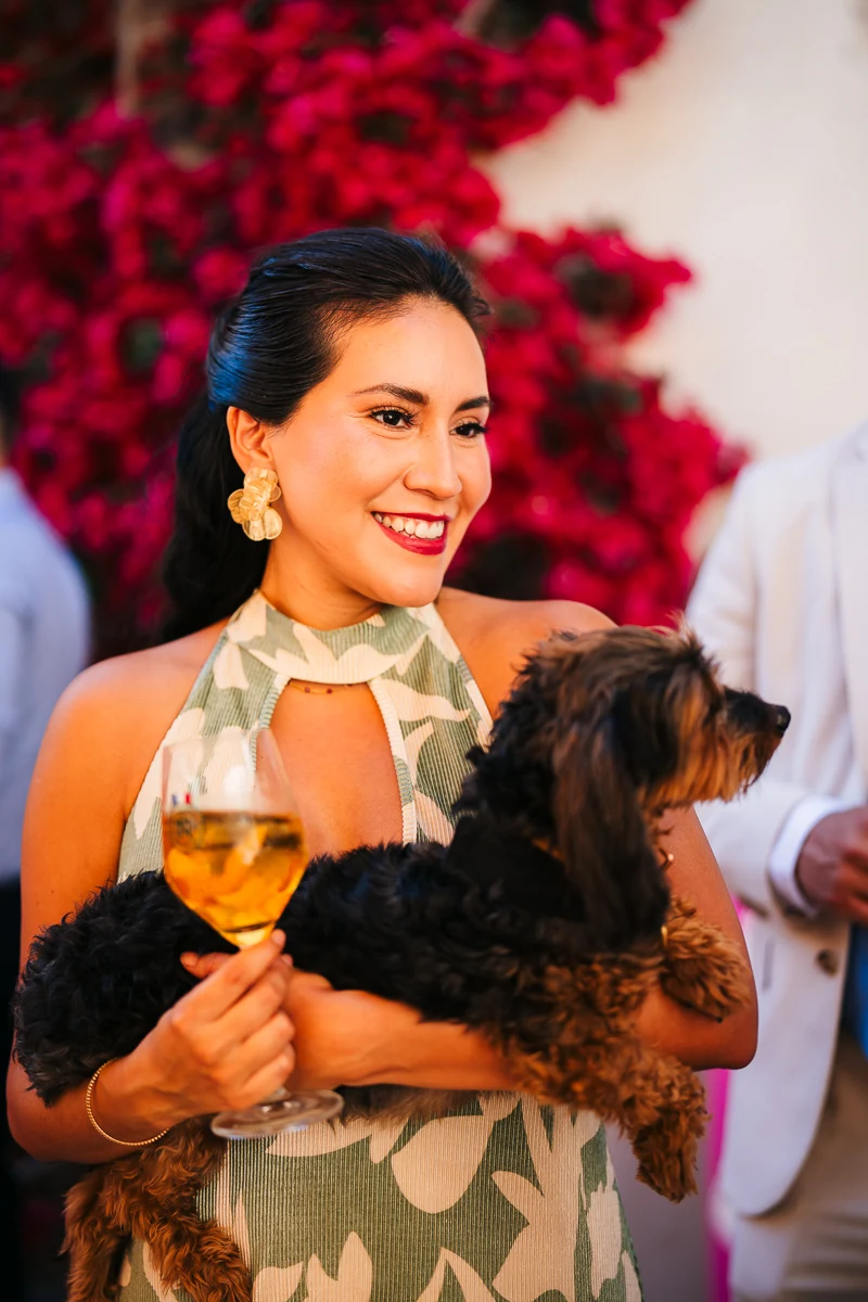 Woman smiling while holding a small dog and a glass of wine