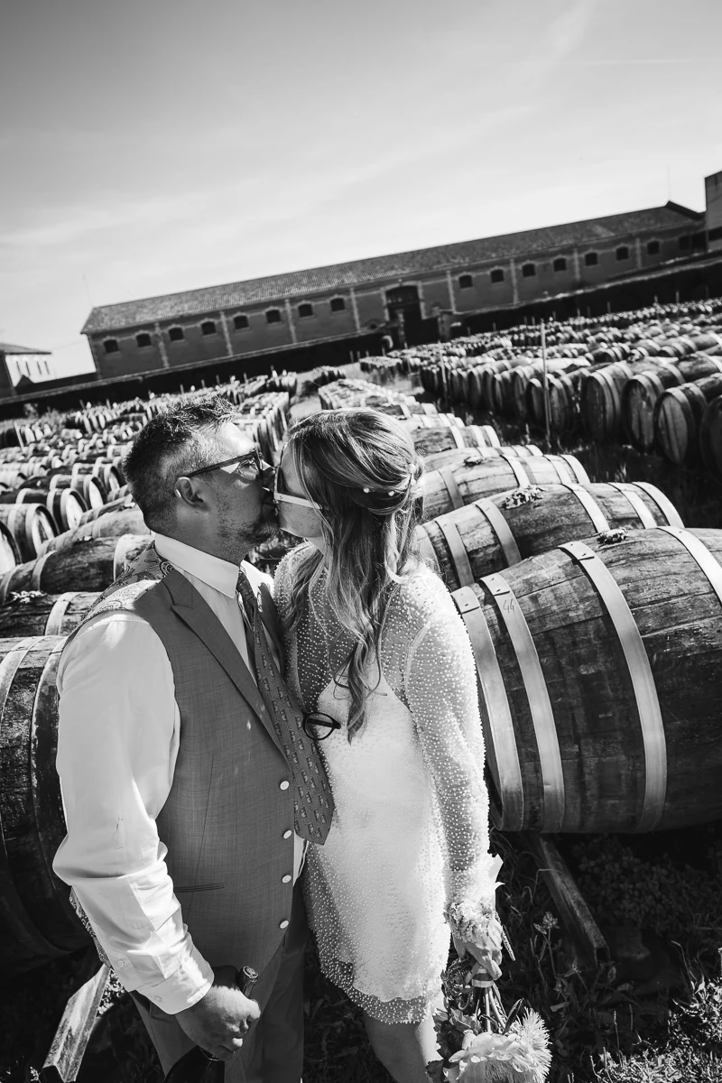 Bride and groom kissing in front of wine barrels at Maison Noilly Prat
