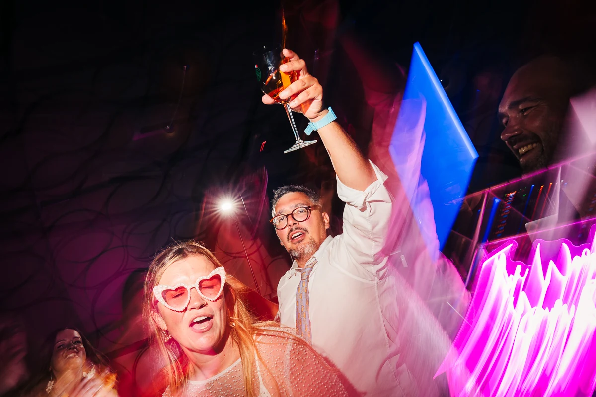 Bride and groom celebrating and raising a glass under colorful dancefloor lights