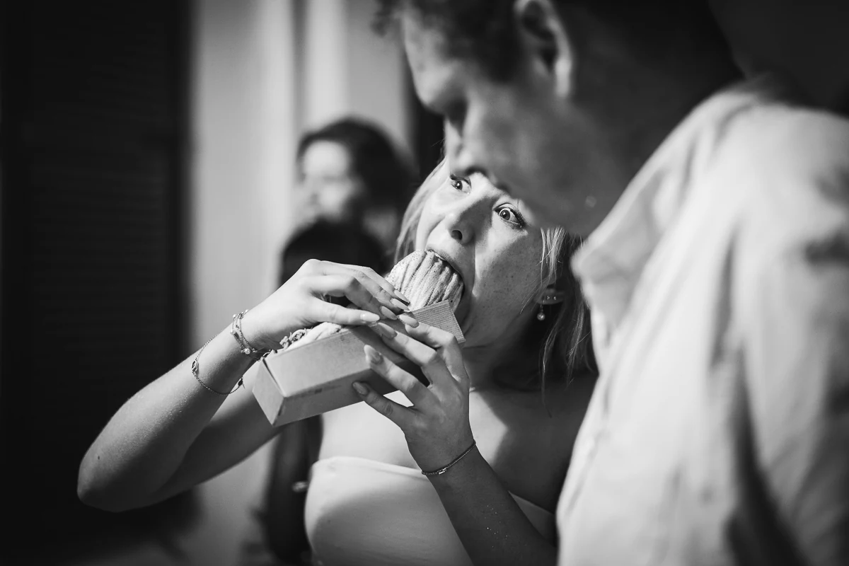 A black-and-white close-up of a guest eating a hot dog late in the evening