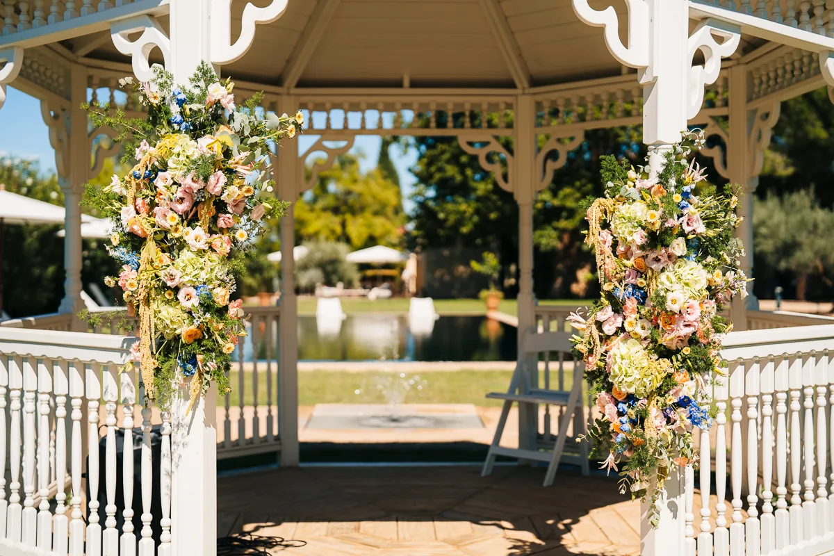 White bandstand with pastel flower arrangements and the pool behind, Domaine de la Trinité wedding