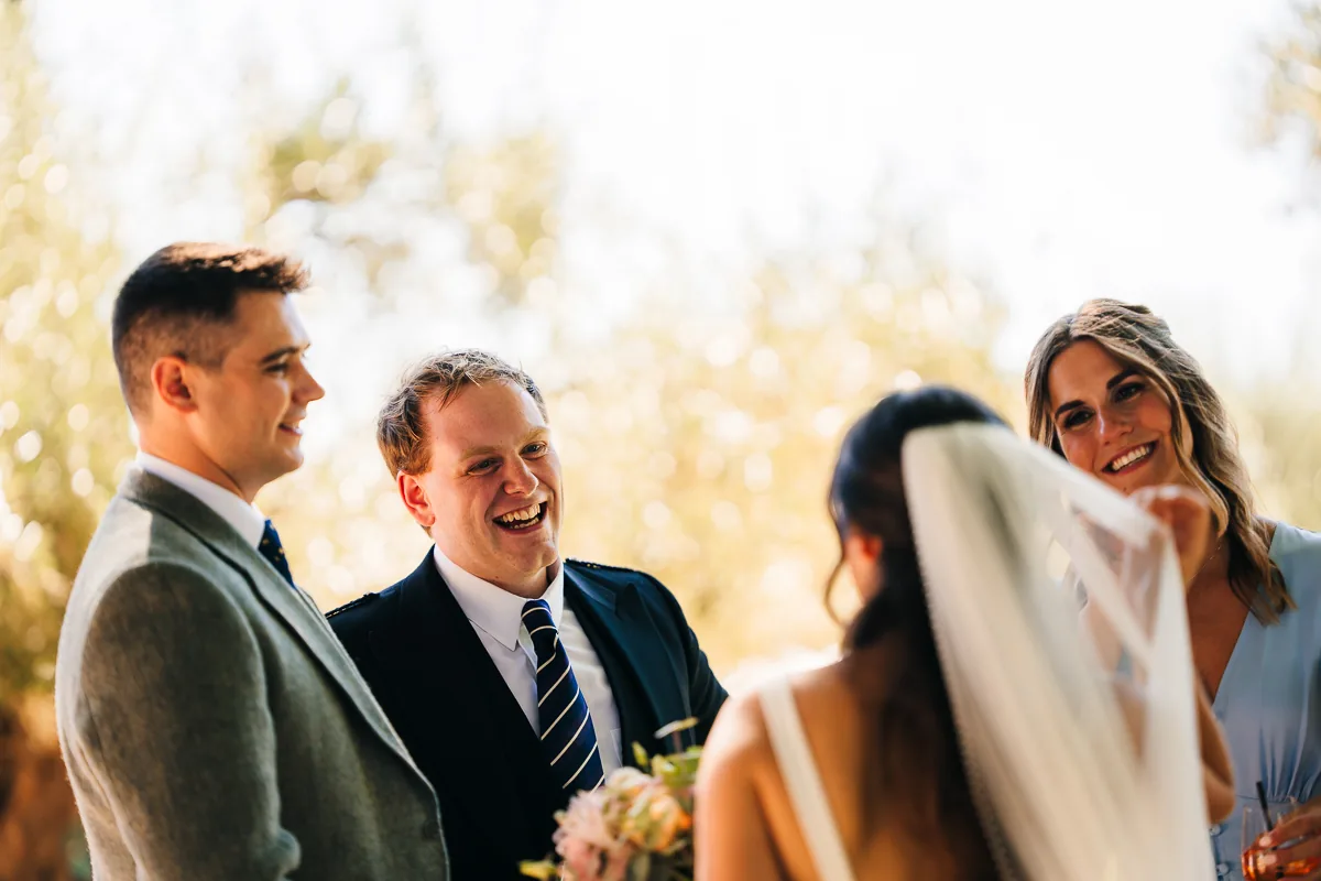 Guests laughing around a bride in her veil during the cocktail hour in the South of France