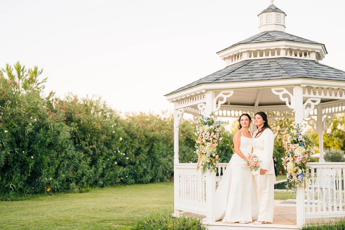 Two brides standing in the white bandstand at sunset in the gardens of Domaine de la Trinité, near Montpellier
