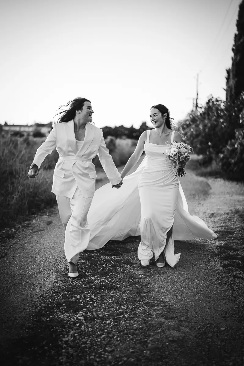 Black and white photo of two brides walking hand in hand on a path at sunset near Montpellier