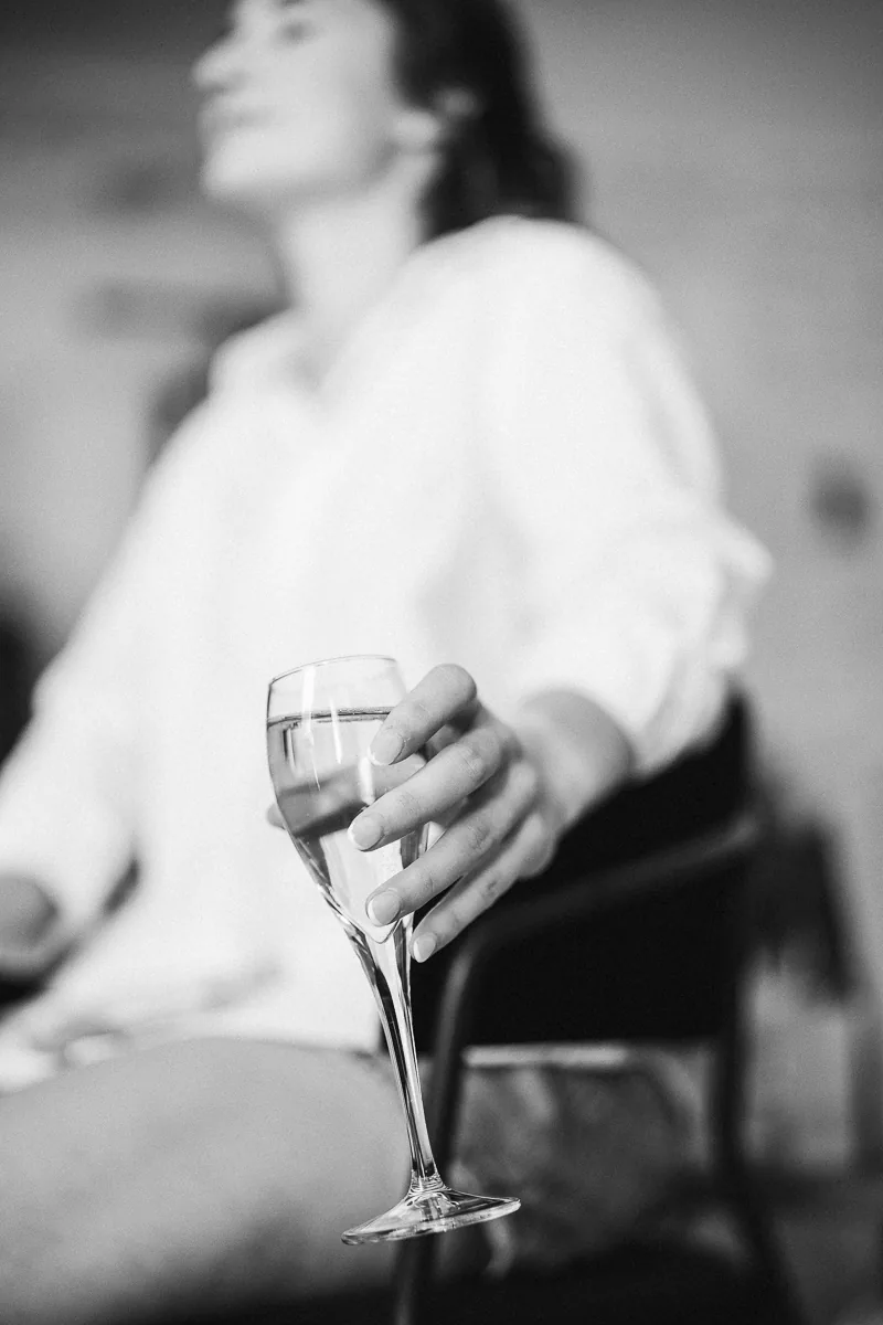 Black and white photo of a bride holding a glass of champagne while getting ready, South of France wedding