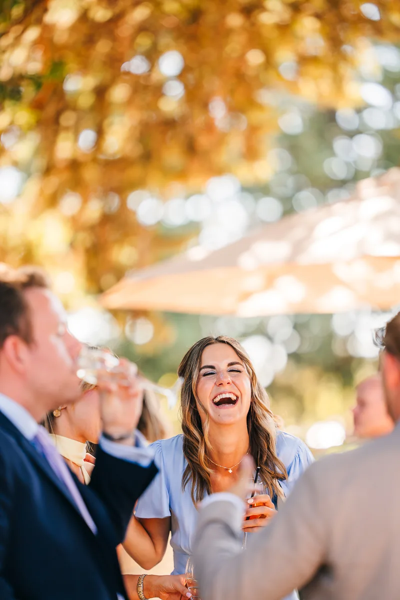 Wedding guest laughing during the cocktail hour under the trees at Domaine de la Trinité