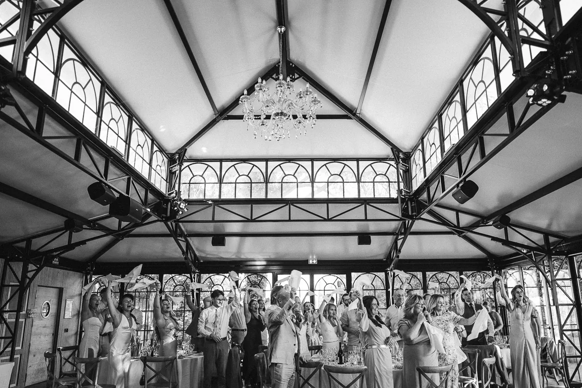 Black and white photo of guests cheering in the orangery as the brides enter, Domaine de la Trinité