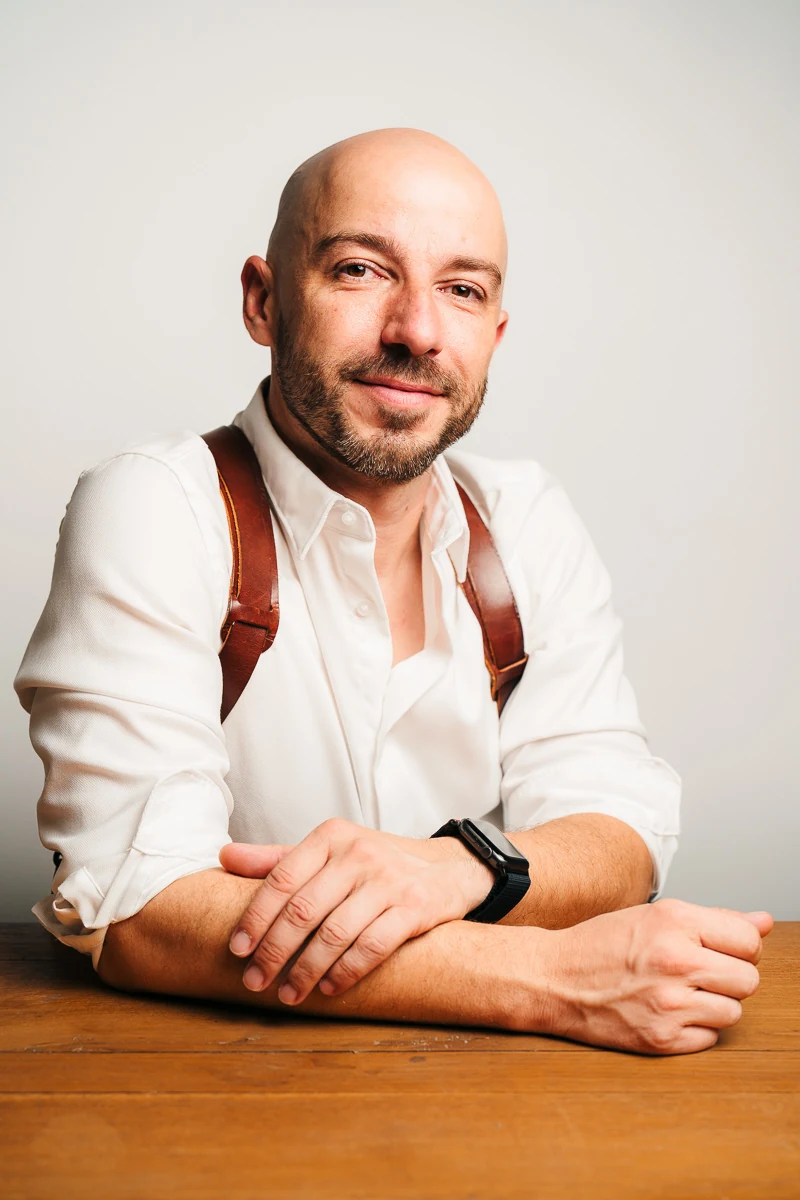 Thibault Maestracci, wedding photographer, leaning on a wooden table and smiling