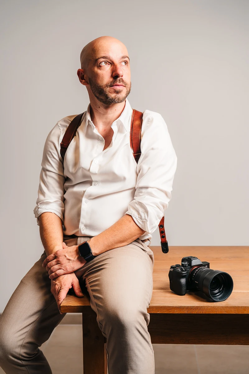 Thibault Maestracci, wedding photographer, sitting on a wooden table next to his camera