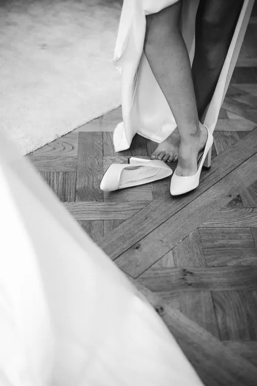 Graphic black and white photo of the bride's feet putting on her shoes, forming a triangle with the white carpet and her veil