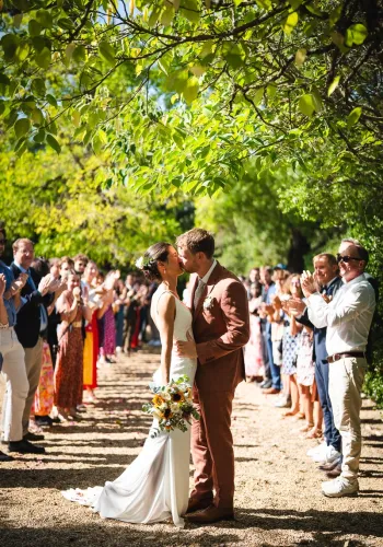 Couple kissing under trees during their guard of honor in warm southern light