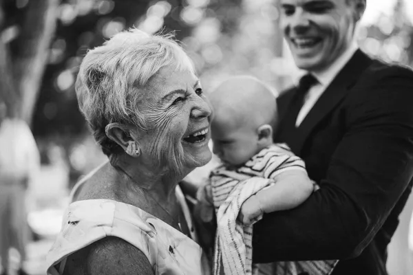 Grandmother laughing joyfully in front of her grandson during a candid wedding moment