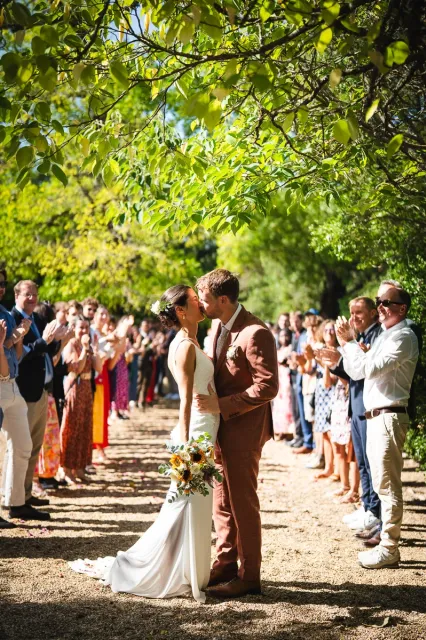 Couple kissing under trees during their guard of honor in warm southern light